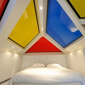 Modernes Schlafzimmer mit weißem Bett und farbenfroher, geometrischer Decke.