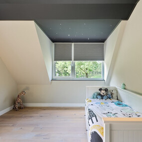 Modernes Kinderzimmer im Dachgeschoss mit Bett, Kuscheltieren und großem Fenster.