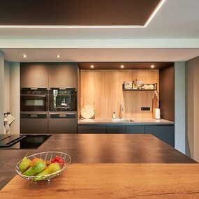 Moderne Küche mit Holzarbeitsplatte, dunklen Fronten und Obstschale auf der Theke.