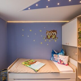 Modernes Kinderzimmer mit gemütlichem Bett, Eulen-Wanddeko und Pflanzen am Fenster.